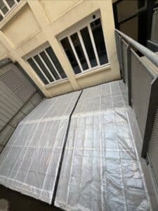 Bâche plastique translucide quadrillée recouvrant une terrasse extérieure devant des fenêtres de bâtiment.