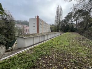 Garages à toits végétalisés devant des immeubles résidentiels et arbres sous un ciel couvert.