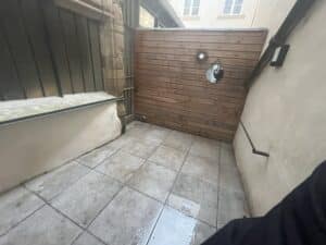 Terrasse carrelée avec paroi en bois et miroirs ronds dans une cour étroite.