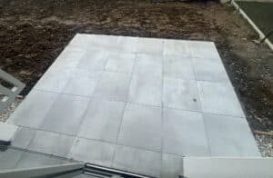 Terrasse moderne en dalles grises carrées sur terre fraîche, aménagement de jardin en cours.